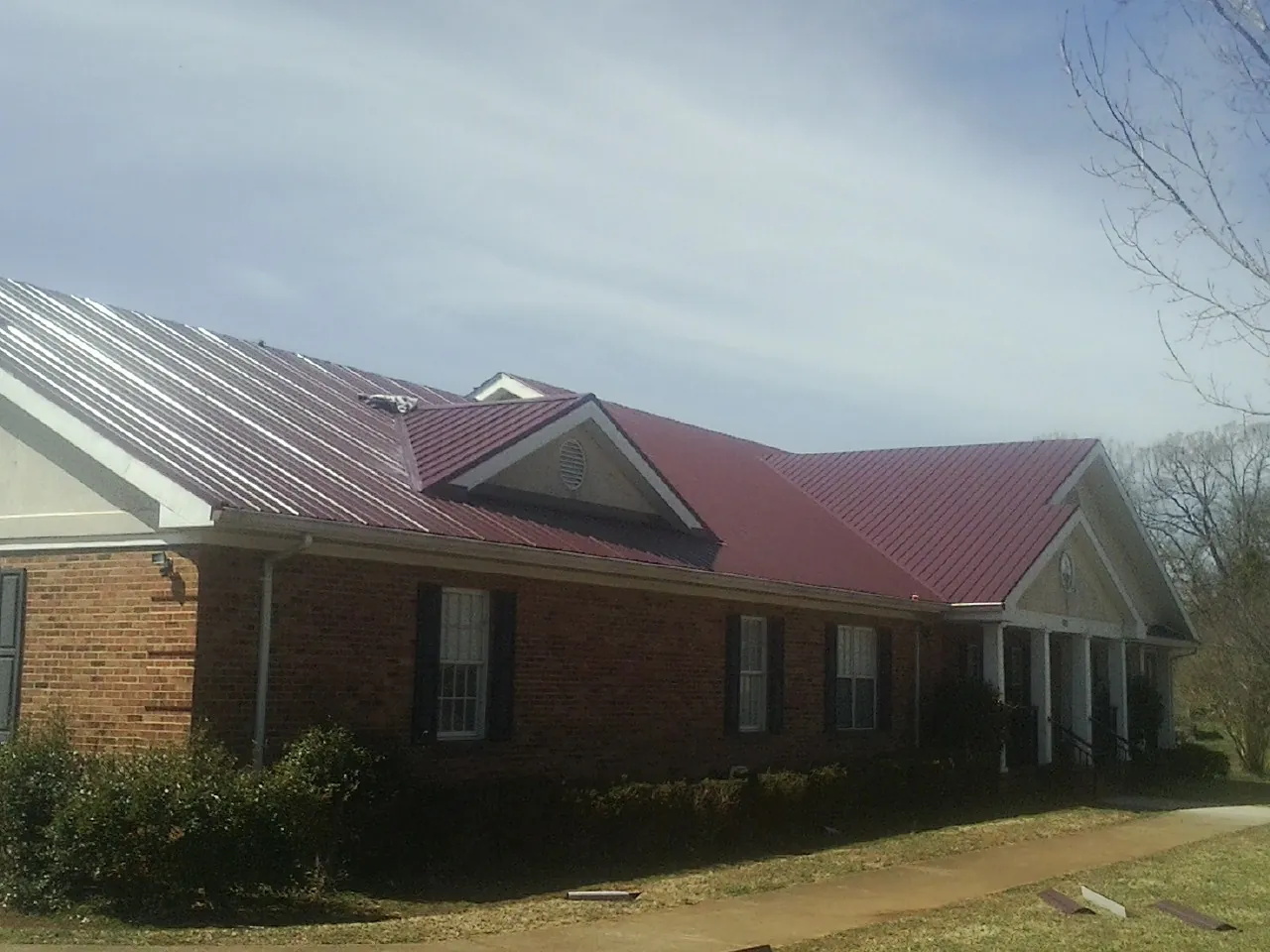 Red metal roof with gabled entries on a long brick building, from a Hail Damage Roof Repair job in Tullahoma