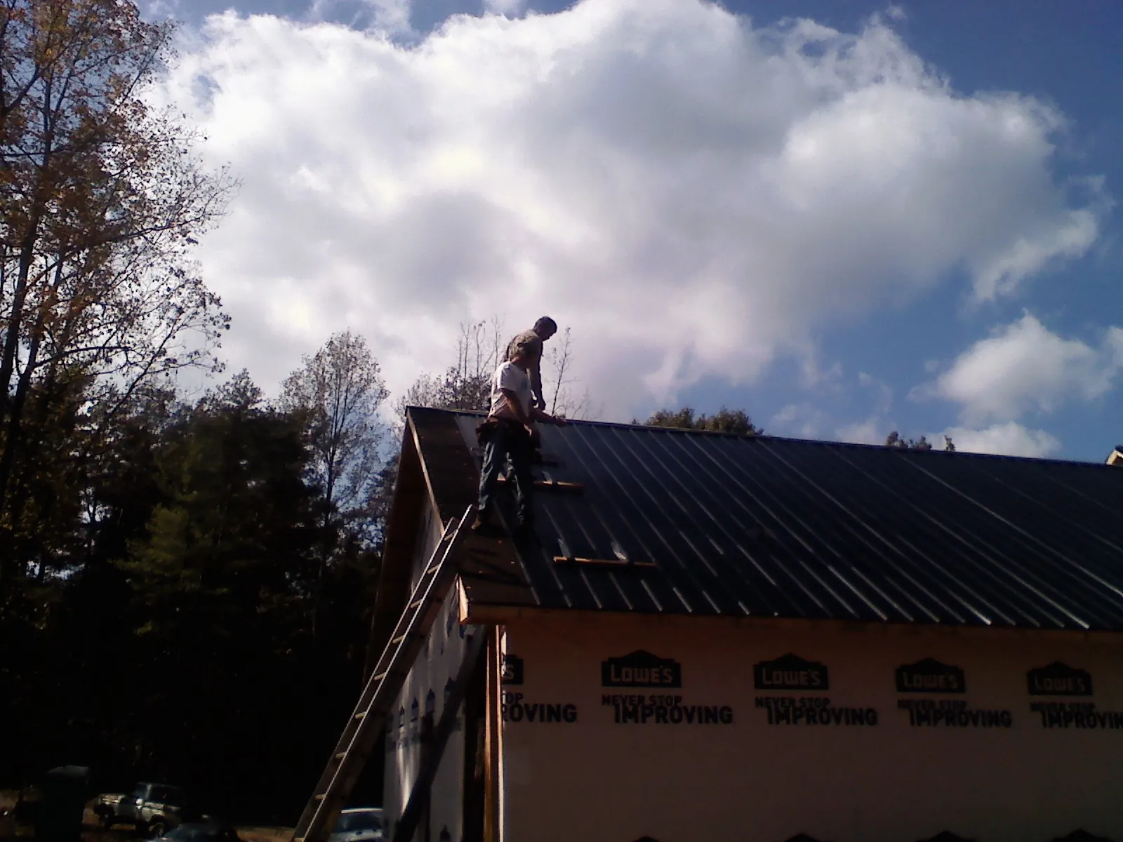 Roofer fastening dark metal panels high against a cloudy sky, from a Roof Inspection job in Tullahoma