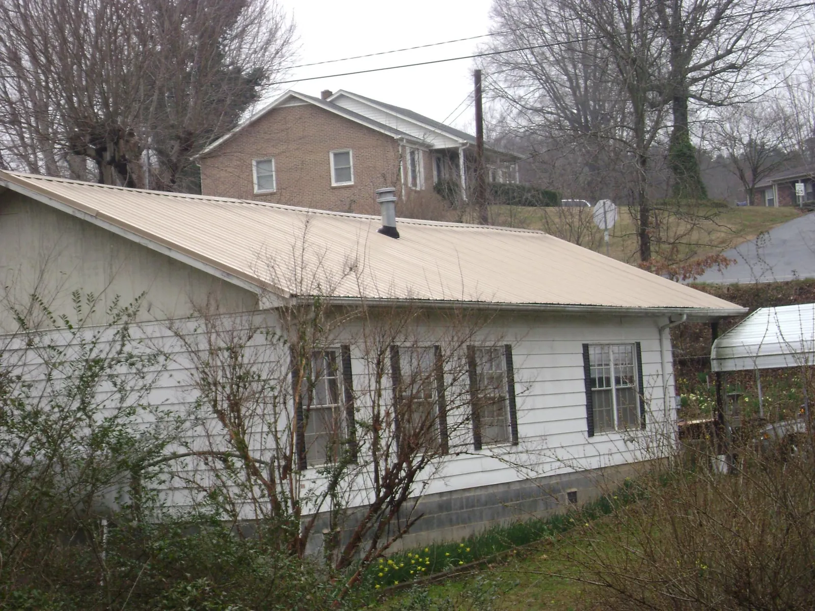 Tan metal roof on a white sided house set into a hillside — Commercial Roofing by Roofing Brothers in Tullahoma